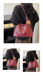 Detail of dark red oversized leather tote bag with zip pocket and bear charm accessory