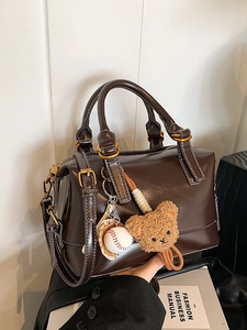 Bolso Boston retro marrón oscuro con dijes de oso y béisbol sobre fondo de libro de moda