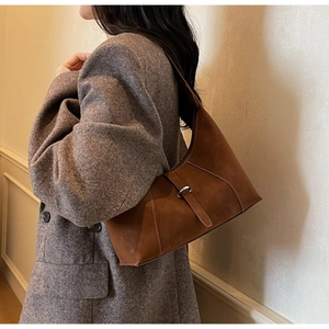 Detail of dark brown matte leather underarm bag with contrast stitching and metal buckle