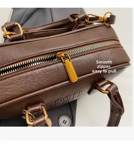 Détail d'un sac à main en cuir marron foncé avec fermeture éclair dorée et poignée lisse