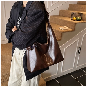 Detail of a dark brown glossy leather tote bag showing a gold logo on a model