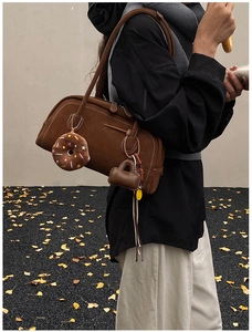 Detailed view of dark brown frosted suede shoulder bag with white stitching and fuzzy charms