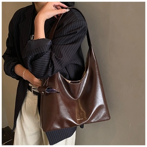 Detail of dark brown tote bag with glossy oil-wax leather texture and chic brand logo