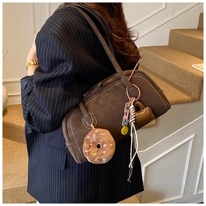 Detail of dark brown matte leather shoulder bag with plush charm and woven accessories