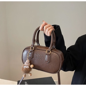 Détail du sac boston en cuir marron foncé avec logo embossé et breloque peluche monstre