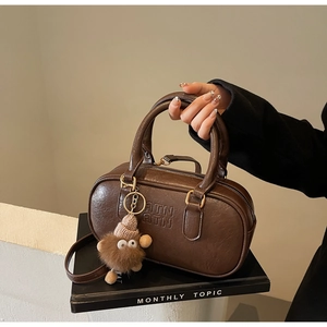 Détail du sac Boston marron foncé avec logo embossé et charm monstre en peluche