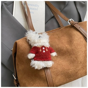 Plush white puppy charm wearing a red sweater hanging on a brown suede tote bag