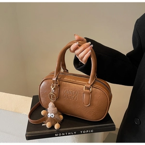 Détail du sac Boston en cuir marron texturé avec logo embossé et pendentif en peluche