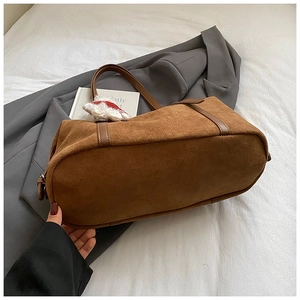 Brown suede tote bag detail with long shoulder straps and a red knit doll charm
