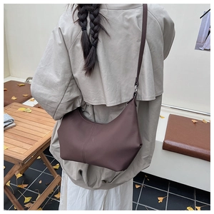 Modèle portant un sac hobo en cuir mat café en extérieur montrant le porté à l'épaule