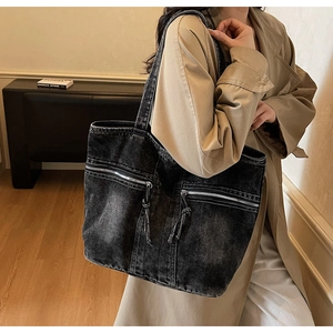 Détail du sac cabas en denim noir avec de longs pompons sur les poches zippées au style rétro