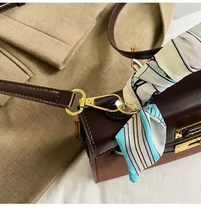Detailed close-up of golden metal hooks and blue striped scarf on brown leather handbag