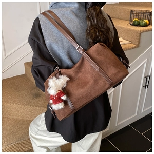 Detail of dark brown suede tote bag with leather strap and a cute white teddy bear charm