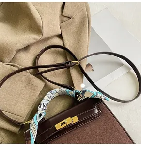 Detail of dark brown leather handbag with scarf-wrapped handle and golden rotary buckle