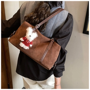 Brown suede tote bag with leather strap and cute bear charm shown on a shoulder