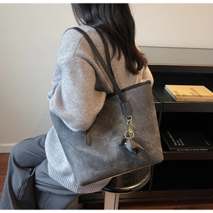 Detail of grey tote bag featuring black leather straps and an elephant charm accessory