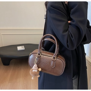 Gros plan du sac Boston marron rétro avec logo ATN gaufré et breloque monstre en peluche