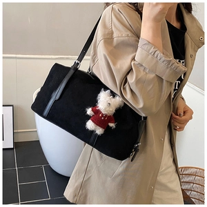 Detail of matte black tote bag with long leather straps and cute plush bear charm