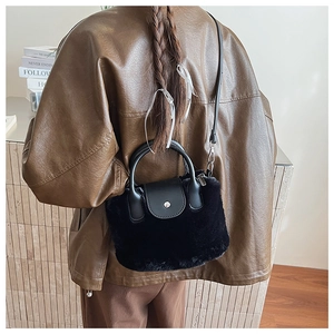 Detail of a small black plush crossbody bag with leather flap shown on a brown jacket