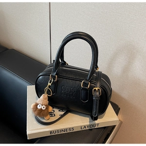 Détail du sac en cuir texturé noir avec ferrures dorées et breloque pelucheuse