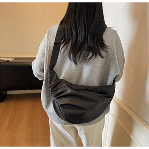 Minimalist black crescent crossbody bag with wide strap shown on model in a cozy indoor setting