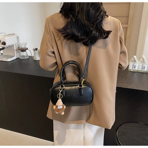 Détail d'un sac bandoulière en cuir grainé noir avec charme de monstre en peluche marron