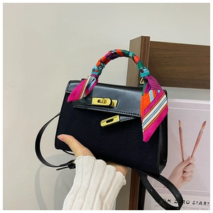 Detail of black trapezoid handbag with gold turn-lock and colorful silk scarf on handle