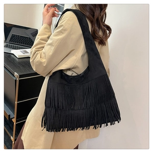 Detail of a black suede hobo bag featuring double tassels and a bohemian shoulder strap