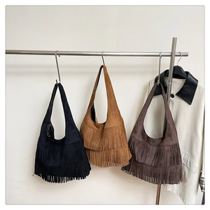 Three bohemian tassel tote bags in black, camel, and brown hanging on a silver rack