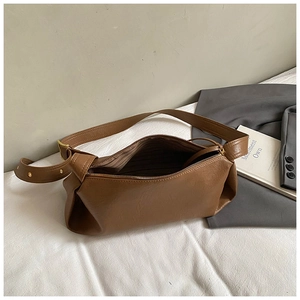 Détail d'un sac baguette marron en similicuir avec zip sur un tissu blanc froissé