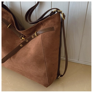 Close-up of brown suede tote bag with leather straps and golden metal hardware details