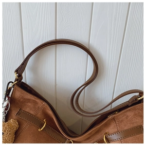 Detail of brown suede tote bag featuring golden buckles, plush bear, and plaid scarf