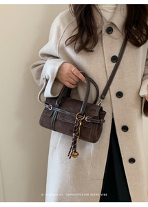 Close-up of retro dark brown suede crossbody bag with decorative bell pendant and handle