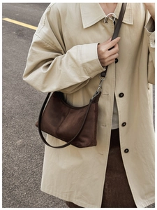 Detail of brown suede tote bag with leather strap and stitching on beige coat