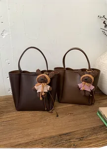 Detail of two coffee brown leather tote bags with cute bear charms on a wooden surface