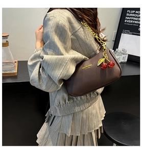 Détail du sac bandoulière marron foncé texture lychee avec chaîne dorée et charm cerise