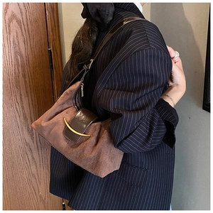 Sac sous le bras en daim marron foncé avec boucle dorée porté sur un blazer à rayures
