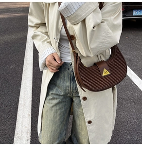 Close-up of brown woven texture and gold triangle buckle on the crescent shoulder bag