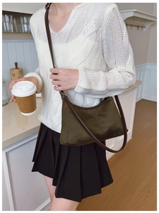 Detail of dark green suede underarm bag with brown leather strap on white knit sweater