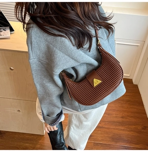 Detail view of woven brown hobo bag with gold triangular buckle worn on shoulder