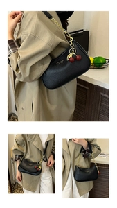 Détail du sac demi-lune en cuir noir grainé avec chaîne dorée et breloque cerise