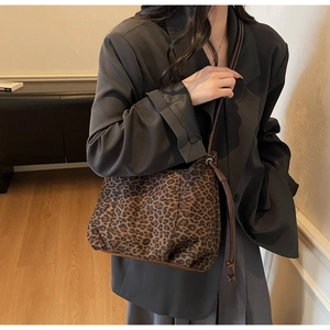Detail of a leopard print tote bag with brown leather strap on a model wearing a blazer