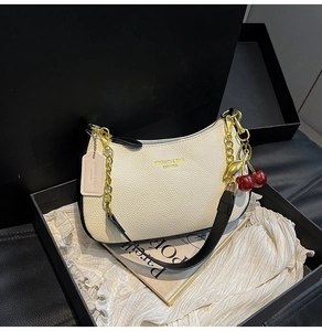 Détail du sac en cuir crème avec chaîne dorée, bordure contrastée et bijou cerise