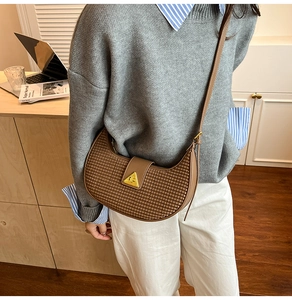 Detailed view of woven texture brown crescent bag with a gold triangular metal buckle