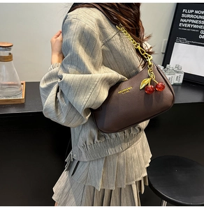 Détail du sac à bandoulière en cuir marron avec chaîne dorée et breloque cerise