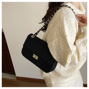 Close-up of black quilted suede shoulder bag with gold chain strap on white knit outfit