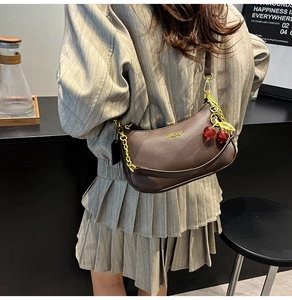 Détail du sac à bandoulière en cuir marron foncé avec pendentif cerise et chaîne dorée