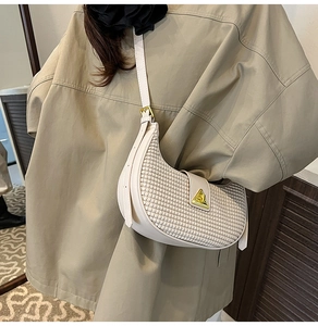 Macro detail of beige crescent shoulder bag featuring woven texture and gold triangle buckle
