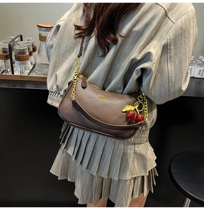 Détail du sac en cuir marron café avec chaîne dorée et breloque cerise sur modèle