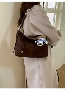 Detail view of brown suede tote bag with metal chain strap and teddy bear charm